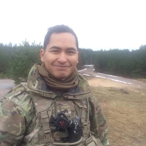 Crisostomo smiles while wearing his uniform, sans helmet, with wilderness in the background.