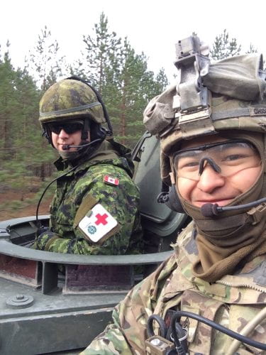 Corey poses for a photo while wearing his full military gear with a member of the Canadian army, also a medic and wearing his full military uniform.