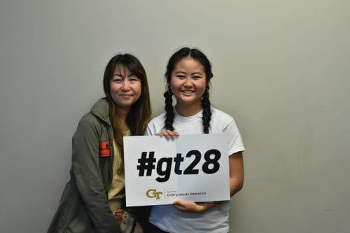 Keiko and Sola Ishibashi stand against a plain wall. Sola holds a sign saying '#gt28'