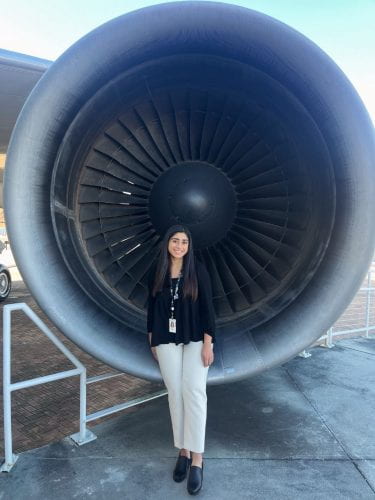 Anna poses in front of a large commercial jet engine
