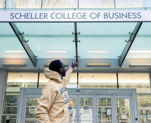 Barrie faces away from the camera to point at the Scheller College of Business sign